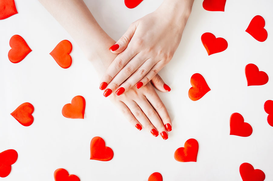 Close-up picture with a woman’s manicured nails in red with hearts in the background